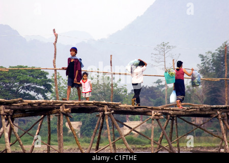 A group of Laotian people are crossing a rural river by walking on a wooden bridge in communist Laos. Stock Photo