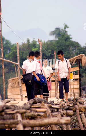 A group of 4 Laotian school children are walking on a wooden foot bridge above a rural river in communist Laos. Stock Photo