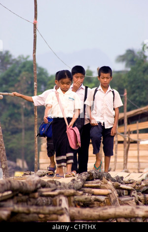 A group of 4 Laotian school children are walking on a wooden foot bridge above a rural river in communist Laos. Stock Photo