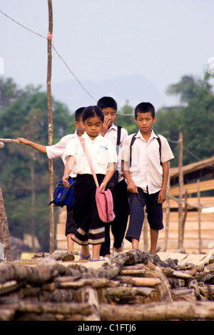 A group of 4 Laotian school children are walking on a wooden foot bridge above a rural river in communist Laos. Stock Photo