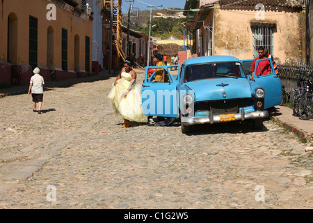 Woman in wedding dress in Cuba leaving blue oldsmobile Stock Photo