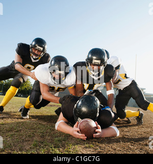 Football players tackling player on football field Stock Photo