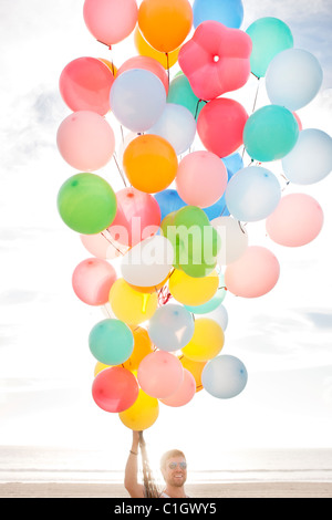 Caucasian man holding balloons on beach Stock Photo