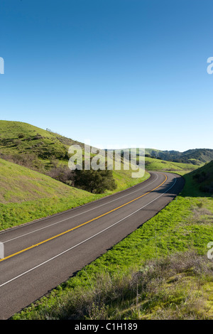 Car vehicle SUV automobile on highway winding through rolling hills covered with green grass and trees. California Highway 1. Stock Photo