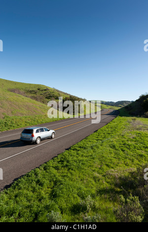 Car vehicle SUV automobile on highway winding through rolling hills covered with green grass and trees. California Highway 1. Stock Photo