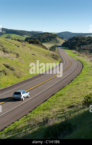 Car vehicle SUV automobile on highway winding through rolling hills covered with green grass and trees. California Highway 1. Stock Photo