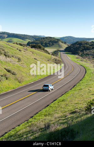 Car vehicle SUV automobile on highway winding through rolling hills covered with green grass and trees. California Highway 1. Stock Photo