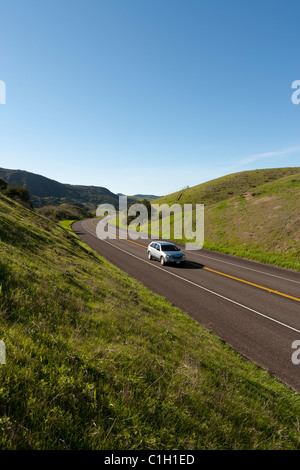 Car vehicle SUV automobile on highway winding through rolling hills covered with green grass and trees. California Highway 1. Stock Photo