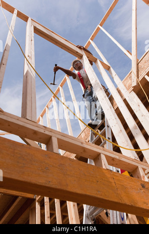 Carpenter using a hammer on the wall frame on the second floor of a house under construction Stock Photo