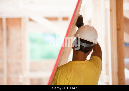 Hispanic carpenter carrying sheathing at a house under construction Stock Photo