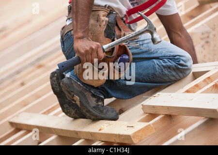 Carpenter with a hammer and tool belt on the roof at a house under construction Stock Photo