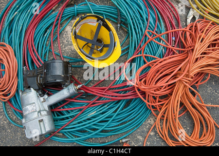 Close-up of power cords and air hoses with a nail gun and a hardhat at a construction site Stock Photo