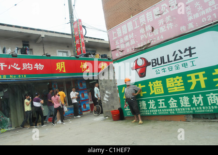 Man wearing hard hat and open shoes. Small stores and advertizements in Pudong, Shanghai, China. Stock Photo