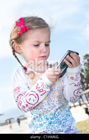A little three year old girl plays with a hand held electronic game. Stock Photo