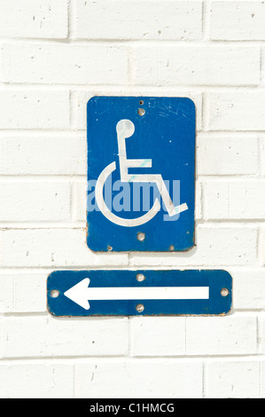 A handicap accessibility sign with direction arrow mounted on a white brick wall. Stock Photo