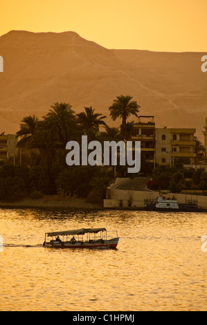 A traditional Egyptian Felucca Boat sails on the Nile in Luxor, Egypt with a passenger ferry passing. Stock Photo
