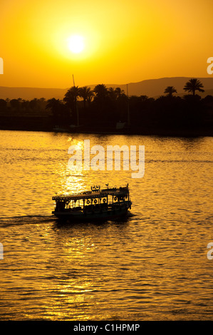 A traditional Egyptian Felucca Boat sails on the Nile in Luxor, Egypt with a passenger ferry passing. Stock Photo