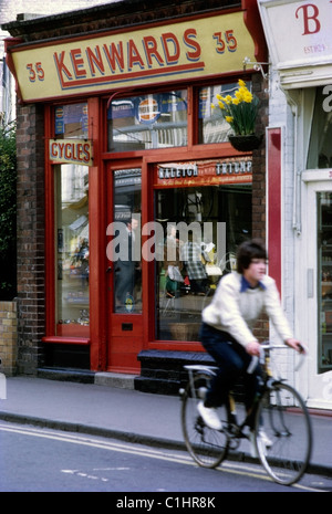 A young teenage boy riding a bicycle past window of  Kenwards Cycle Shop in Royal Tunbridge Wells, Kent England UK 1970s 1972  KATHY DEWITT Stock Photo