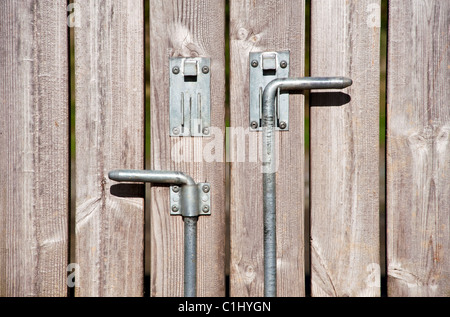 Bolts on a pair of large, wooden panel gates. One bolt has been raised, the other is in the ground and holding the gate Stock Photo