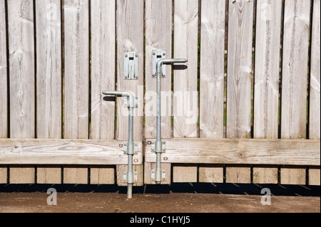 Bolts on a pair of large, wooden panel gates. One bolt has been raised, the other is in the ground and holding the gate Stock Photo