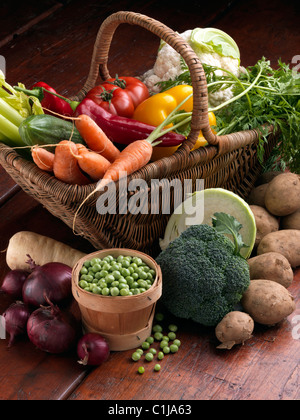 Wicker basket raw vegetables tomatoes sweet red yellow peppers carrots peas cauliflower parsnips broccoli cooking ingredients Stock Photo
