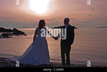 This lovely photo is a silhouette of a bride and groom holding hands at sunset on a beach overlooking the ocean. Stock Photo