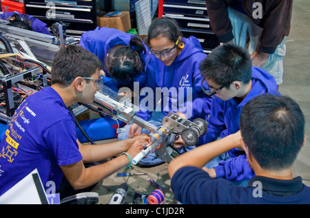 This image shows multi ethnic teen girls and guys working as a team on a robot, wearing safety glasses. Robotic competition. Stock Photo