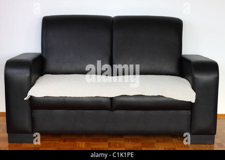 Black leather modern sofa on hardwood against white wall Stock Photo