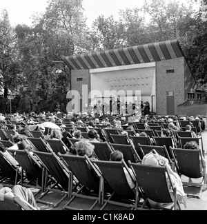 1950s, a photograph by J Allan Cash of people sitting in deck chairs at a bandstand on Victoria Embankment Gardens enjoying a summer concert. Stock Photo
