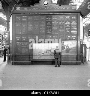 1950s, a man studies the large departure board for the train times of the International European Express trains at Victoria railway Station, London. Stock Photo