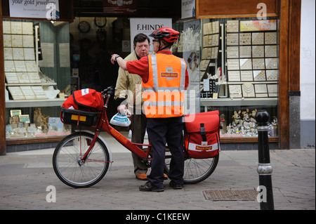 Postman with a bicycle giving directions to a passerby on his town centre round Stock Photo