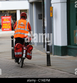 Postman riding a bicycle with pannier bags on his town centre round in Evesham England UK Stock Photo