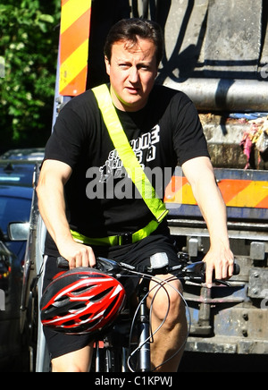 David Cameron jumps on his bike without wearing his helmet after dropping his children off at school, but struggles to get Stock Photo