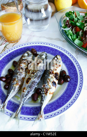 On the table, grilled mackerels poured with olive oil, orange juice and bread. Stock Photo