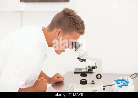 Laboratory work: young researcher looks in microscope and takes notes Stock Photo