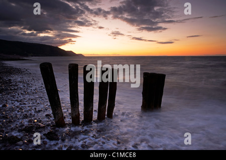 Sunset over wooden groynes on the seafront at Bossington beach on the Exmoor coastline Somerset UK Stock Photo