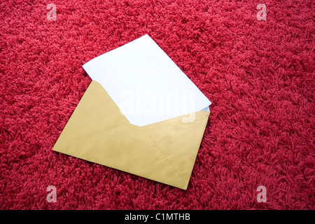 Blank letter inserted in old envelope on red rug Stock Photo