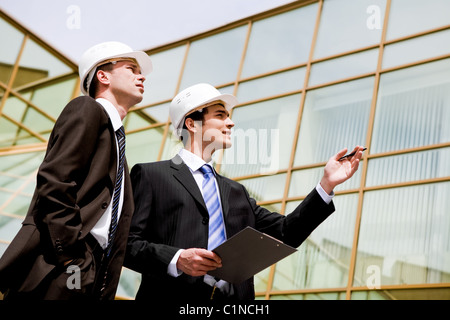 Photo of two co-workers looking at new building while one of them pointing at it Stock Photo