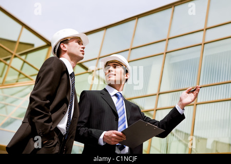 Photo of two co-workers discussing new project with modern building at background Stock Photo