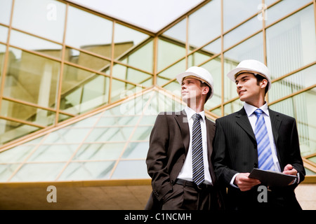 Photo of young engineers looking aside with modern building at background Stock Photo