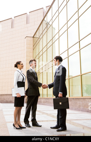 Portrait of two businessmen shaking hands after signing contract with pretty employee standing near by Stock Photo