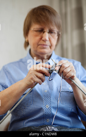 Elder woman doing knitting at home, focus on hands and needles Stock Photo