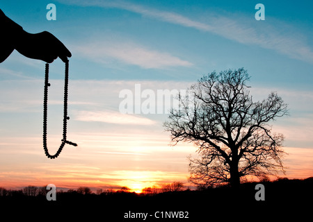 Hand holding rosary, silhouetted against a nice sunset Stock Photo