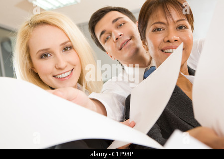 Front view of happy co-workers looking at camerea with smiles and giving papers Stock Photo