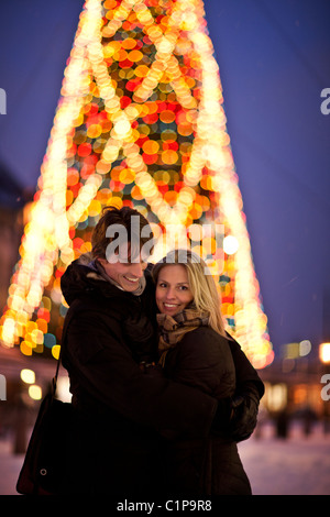 Couple standing in front of illuminated Christmas tree Stock Photo