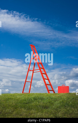 Red ladder and red briefcase in grass  field against blue sky Stock Photo