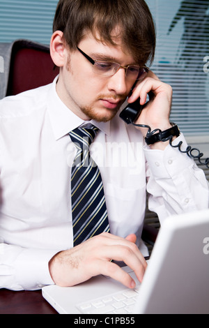 Portrait of busy boss talking on the phone while typing important documents Stock Photo