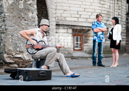 Musician plays a guitar on the streets of Tallinn. A couple enjoys listening his music. Stock Photo