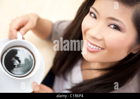 A beautiful young Chinese Asian Oriental woman with a wonderful toothy smile drinking tea or coffee from a white cup and saucer Stock Photo