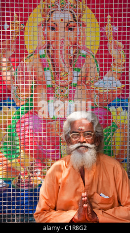 Sadhu or holy man in front of poster of Hindu god Ganesh in Kerala's capital of Trivandrum. Stock Photo